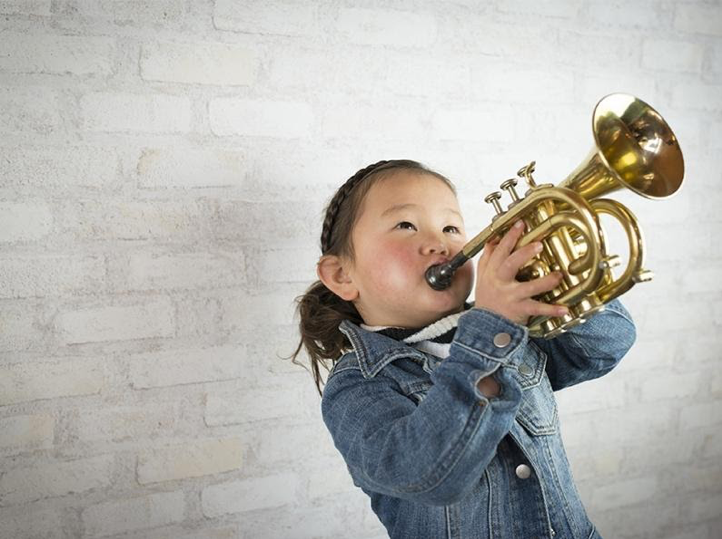 A young girl plays a horn instrument.]