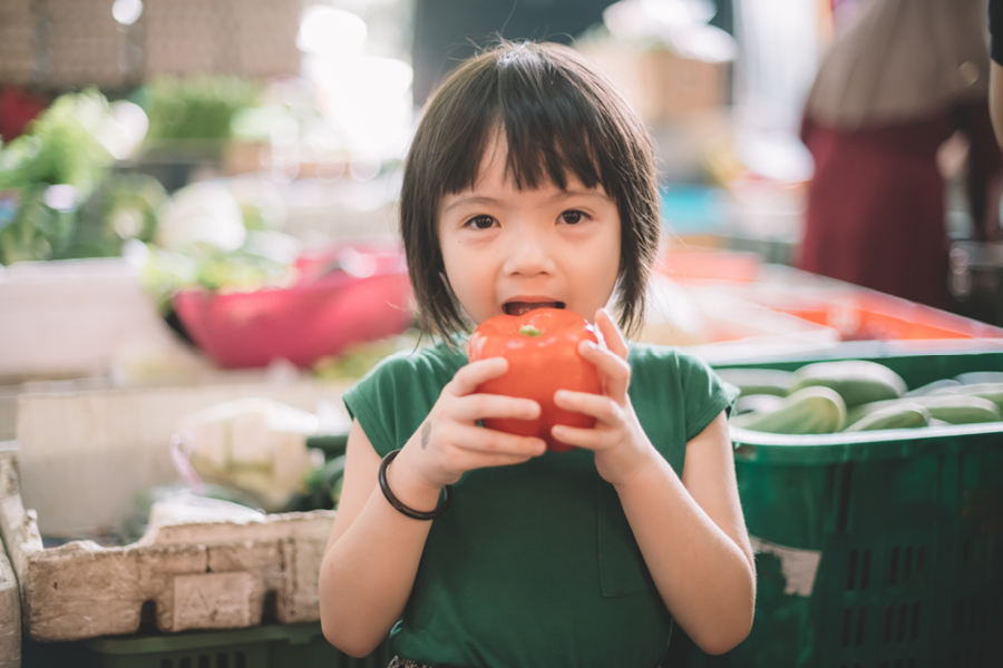 Child smiling and eating an apple at the farmers market.