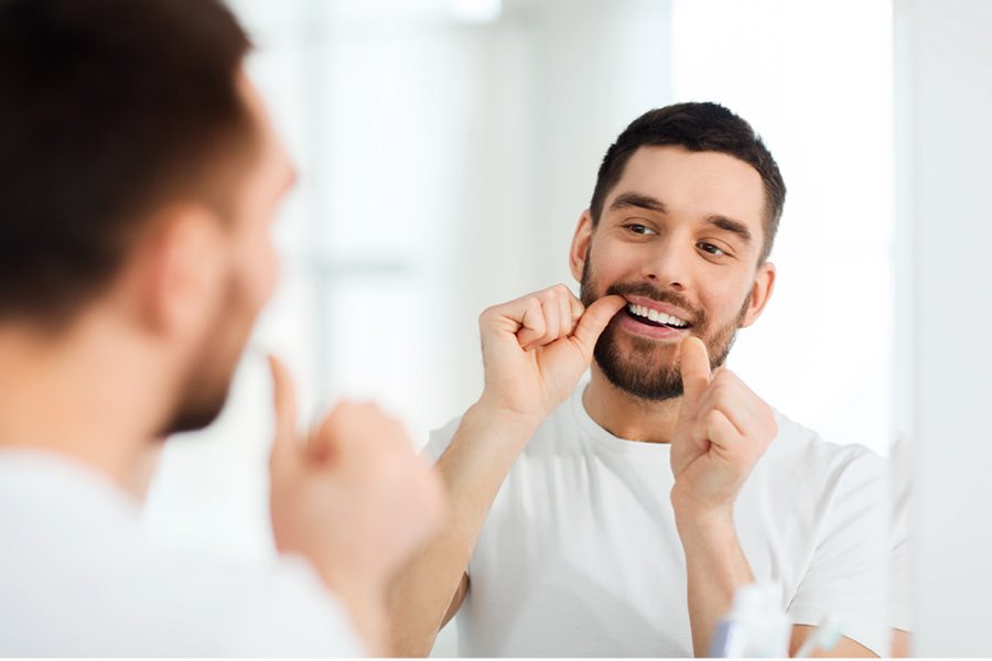Person flossing their teeth in the bathroom mirror.